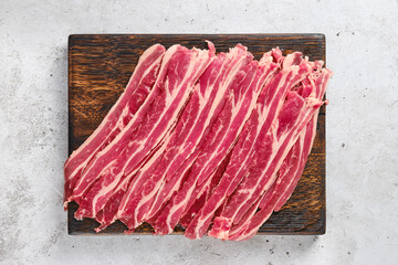 Top view of wooden cutting board with raw beef bacon strips