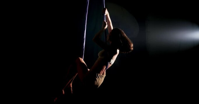 A young adult woman performs acrobatic exercises on the canvases and spins