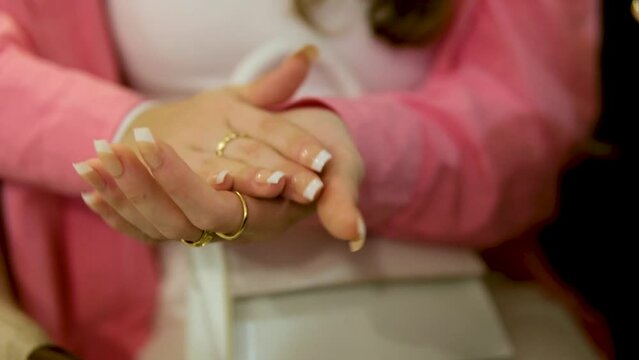 hands of a young woman of a young girl Applause clap hands close-up French manicure long nails well-groomed hands gold rings pink shirt white. Handbag and light clothes