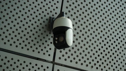 Black surveillance camera mounted on perforated steel plate tile wall