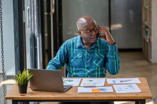 A black senior man in casual cloths using a mobile phone to discuss new season projects and business performance forecasts.