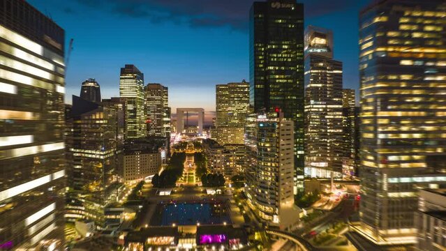 Aerial hyperlapse footage of modern La Defense district at dusk. Forwards fly above busy multilane road in evening city. Paris, France