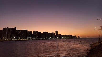 Beachfront twilight in Fortaleza; city lights and azure waves under a soft pink sky