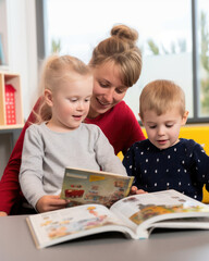 jeunes enfants qui lisent un livre en compagnie d'un adulte dans une biblioth&egrave;que