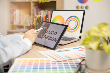 Designer creating graphic logo on a table using tablet and laptop - obrazy, fototapety, plakaty