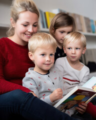 jeunes enfants qui lisent un livre en compagnie d'un adulte dans une bibliothèque