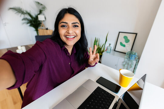 Happy indian woman taking selfie portrait while studying on laptop at home. Education and technology concept.