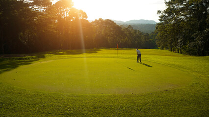Golfer playing golf in the evening golf course, on sun set evening time.