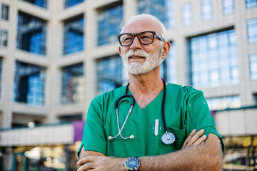 Portrait of a successful mature doctor with a beard and in a medical uniform, outside a modern...