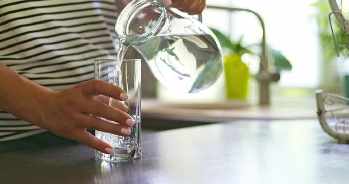 Close up of woman pouring fresh clean water into glass from jug at home