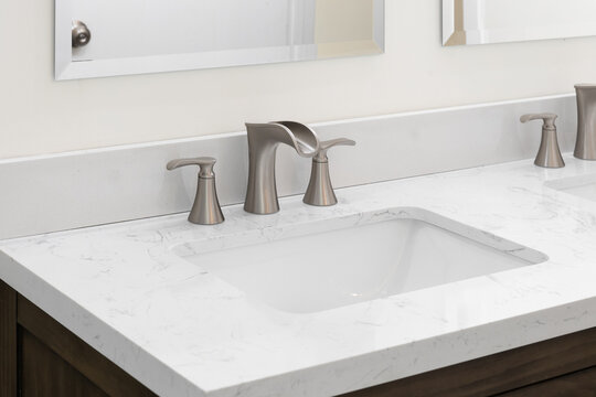 A bathroom faucet detail with a bronze widespread faucet, white marble countertop, and a dark wood cabinet.
