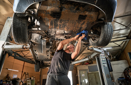 Repairman, worker repairing car, holding rag, wiping. Strong, hardworking man working in servicing center, mainteining automobiles. Concept of manual labor.