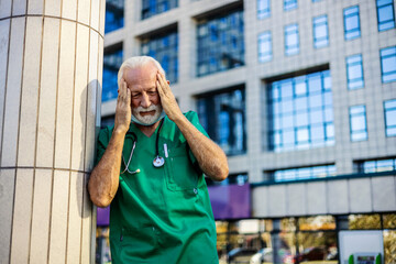 Fototapeta premium Tired exhausted Caucasian male doctor wears green uniform standing in front of hospital.