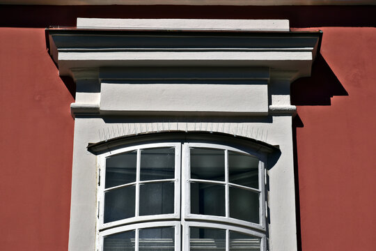 closeup view of old style wood bow window. stucco exterior wall. arched shape. outer operable leaf on hinges. strong light. European architecture. smooth stucco wall. white trim. sharp bird repellent