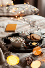 warm cozy bedroom interior with cup of hot chocolate on tray, candles christmas lights
