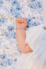 A close-up of a baby's hand with her fist balled up. She lies on a blue floral sheet