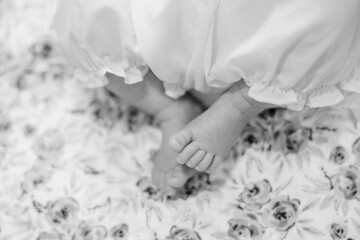 A close-up of a newborn baby feet and toes. She wears a long white dress