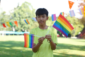 Asian boy holds a rainbow flag in front of a house decorated with rainbow flags during Pride Month to show LGBT pride and identity. Soft and selective focus. 