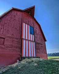 A wooden barn with a door with the American flag design, with grass in front of it on a sunny day © Wirestock