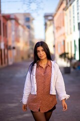 Young Hispanic Woman Walking In City With White Jacket And Brown Shirt