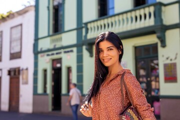 Smiling young hispanic woman looking at camera walking down street