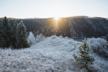 Morning sunrise on the mountain, the glare of the sun shining directly into the camera, the winter landscape, the first snow in the mountains, the hilly terrain, the ground covered with frost.