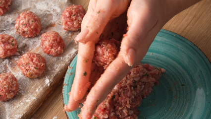 Hands press and roll a seasoned ground meat mixture, preparing meatballs.
