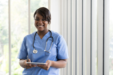 Portrait of happy and smiling African American young female doctor wearing blue scrubs uniform and...
