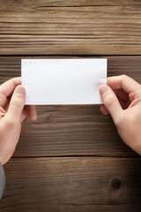 Obraz premium Man's hands holding a blank sheet of paper on a wooden background.