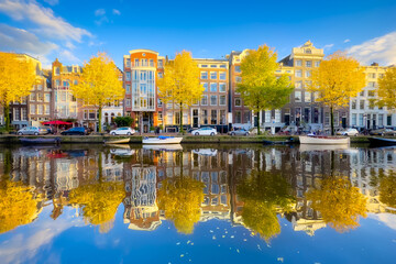 Amsterdam in the fall time.  Capital of the Netherlands. View of old houses and the canal. Reflection on the surface of the water. Yellow leaves on the trees. Postcard, background or wallpaper. - obrazy, fototapety, plakaty