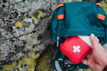 Hand taking out first aid kit from hiking backpack, red first aid kit on a journey, concept of an...
