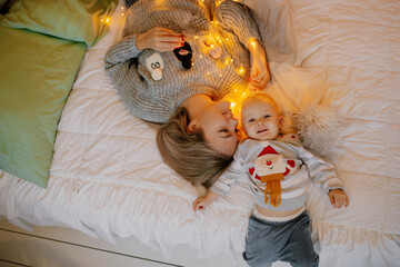 Child in christmas pajamas with mom on bed with garlands