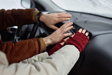 Young couple in winterwear holding hands by warm air blowing from car stove while sitting on front seat during family travel in winter