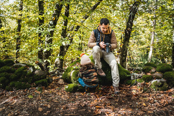 Photographer father with backpack and his fashionable son with hat resting sitting on a stone in...