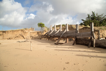 Érosion côtière suite à une tempête : recul de la dune et épi de protection endommagé....