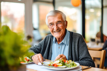 Senior man in a retirement home happily enjoying a healthy lunch. A showcase of a lifestyle of...