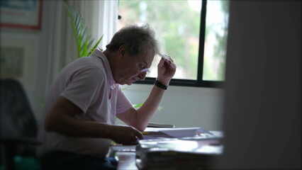 Candid senior man working at home inspecting documents concentrated reading paperwork. Older person in office desk
