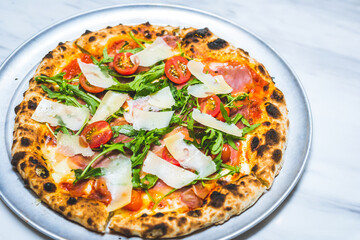 Neapolitan style pizza with cheese, patma ham, arugula, tomato sauce and cherry tomatoes