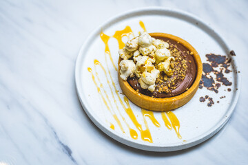 chocolate tart with biscuit base, chocolate ganache, popcorn and caramel sauce