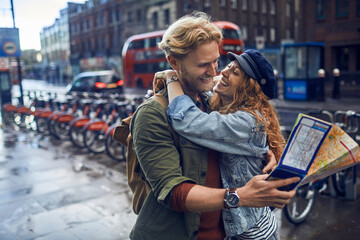 Happy young couple of travelers holding map in the city