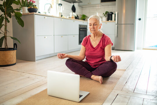 Senior woman practicing yoga in front of laptop at home