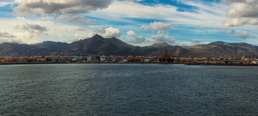 Panoramic landscape view of international commercial harbor with moored ships in Palermo, Italy. City and picturesque mountain range in the background. Travel and tourism concept