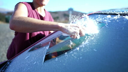 Close-Up Hand Clearing Frost for Winter Road Trip Commute in the morning. Prepping Car Windshield with Ice Scraper