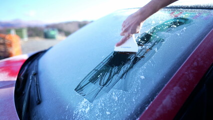 Close-up hand Removing frost from car windshield glass with ice scraper, preparing for road trip...