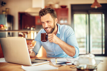 Happy young man holding coffee cup looking at laptop in home setting