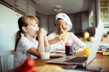 Little daughter using laptop with mother on dining table during breakfast at home