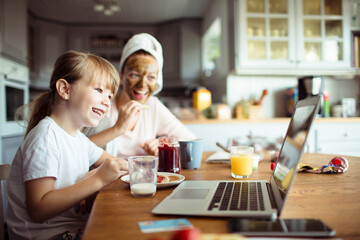 Little daughter using laptop with mother on dining table during breakfast at home