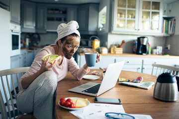 Young woman eating healthy breakfast in the morning using laptop at home - Powered by Adobe