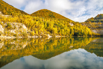 Naklejka premium Autumn landscape with reflection of colorfull hills in the lake. Flooded quarry near the village Sutovo in Slovakia, Europe.