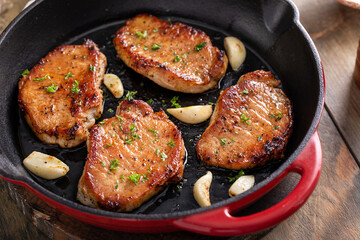 Pork chops seared in a cast iron pan with garlic